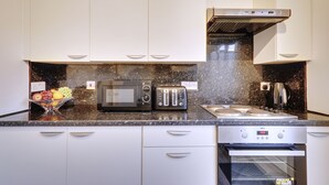 A modern kitchen with white cabinets, a granite countertop, a microwave, a toaster, a kettle, and an oven. - Walter Place (Edgware)