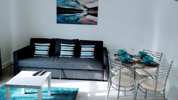 A modern living room with a grey sofa, a white coffee table, and a dining table set with blue bowls and glasses. - Walter Place (Edgware)