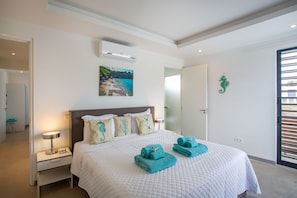 Un lit bien fait, recouvert d’une couette blanche, avec deux serviettes enroulées et une décoration représentant un hippocampe accrochée au mur.
