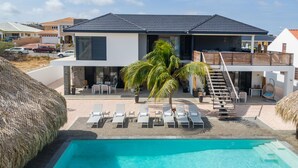 A modern two-story house with a swimming pool, outdoor seating, and a staircase leading to a balcony. - Villa Hasta La Vista Royal (Jan Thiel)