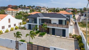 A modern two-story house with a flat roof, a balcony, and a paved driveway. - Villa Hasta La Vista Royal (Jan Thiel)