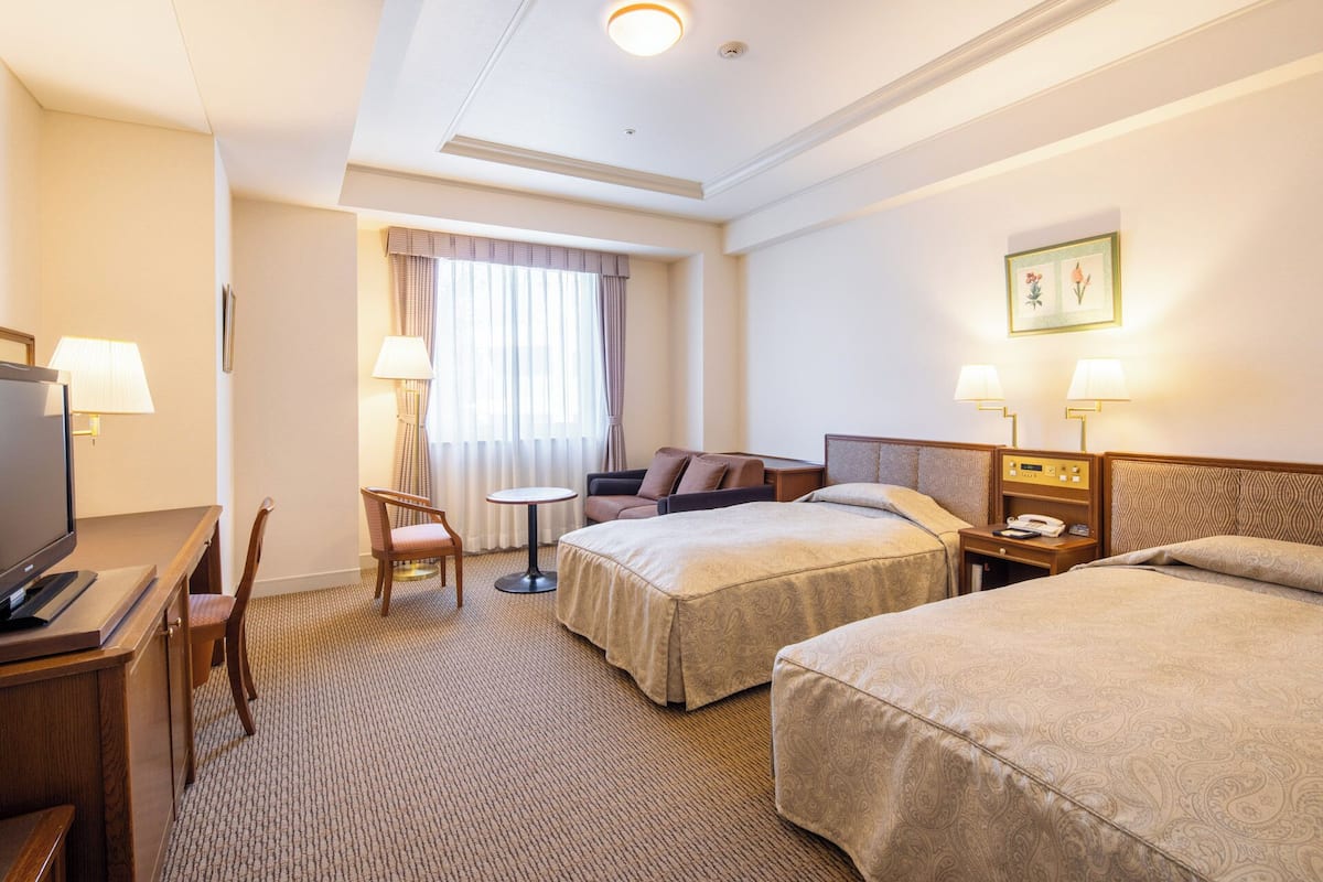 Une chambre d’hôtel avec deux lits, un bureau avec une télévision, une chaise, une petite table et une lampe.
