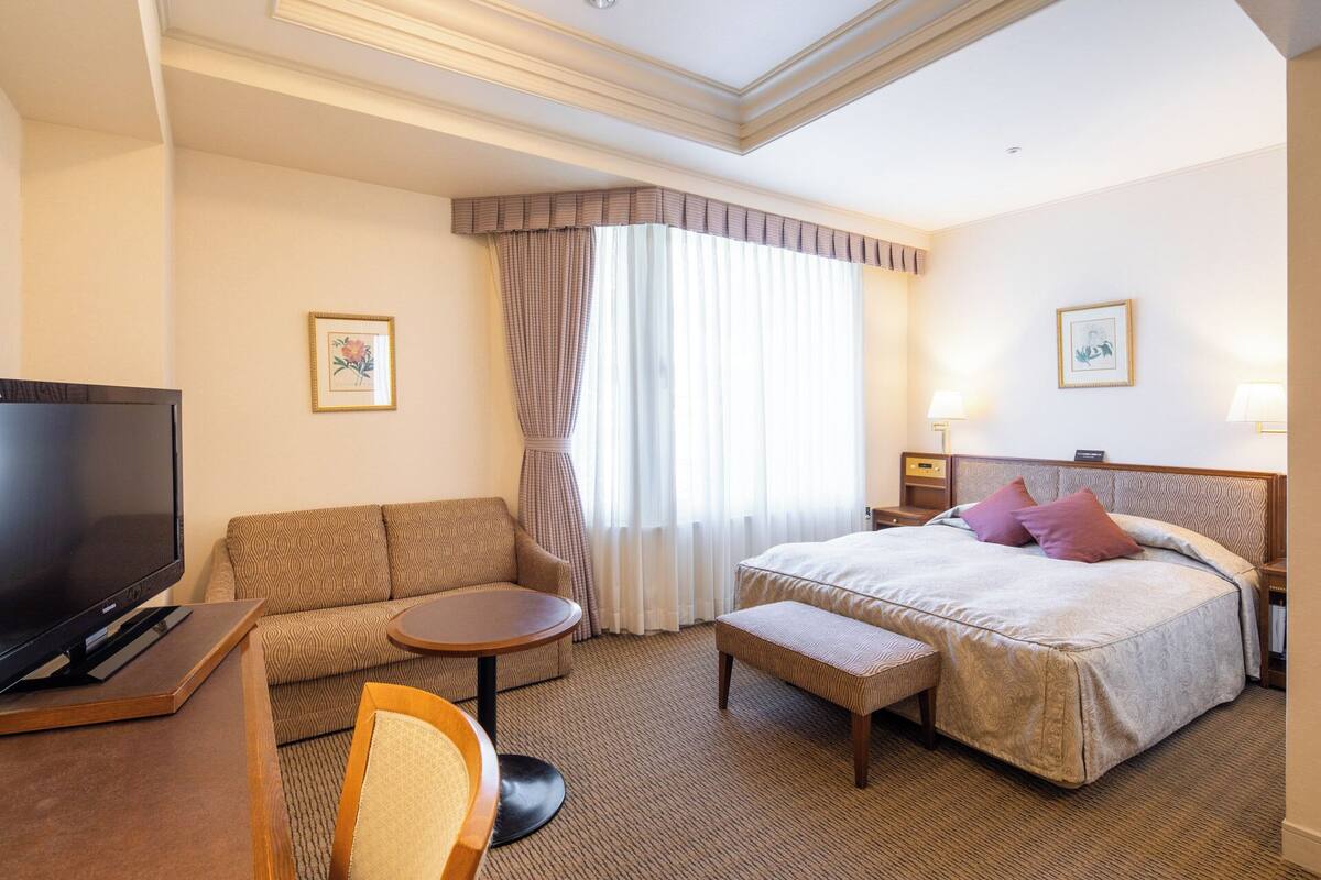 Une chambre d’hôtel avec un lit, un canapé, une télévision, une petite table et un banc.