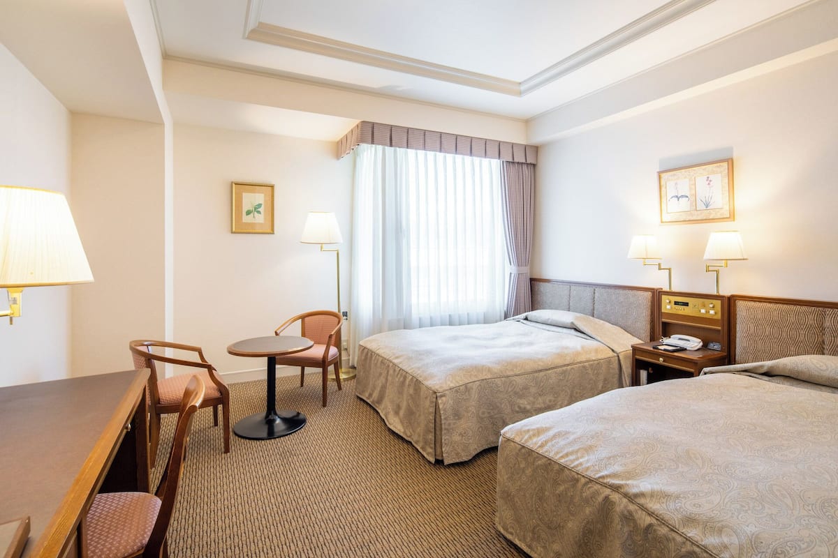 Une chambre d’hôtel avec deux lits, un bureau, une chaise, une lampe et une table de chevet avec un téléphone.