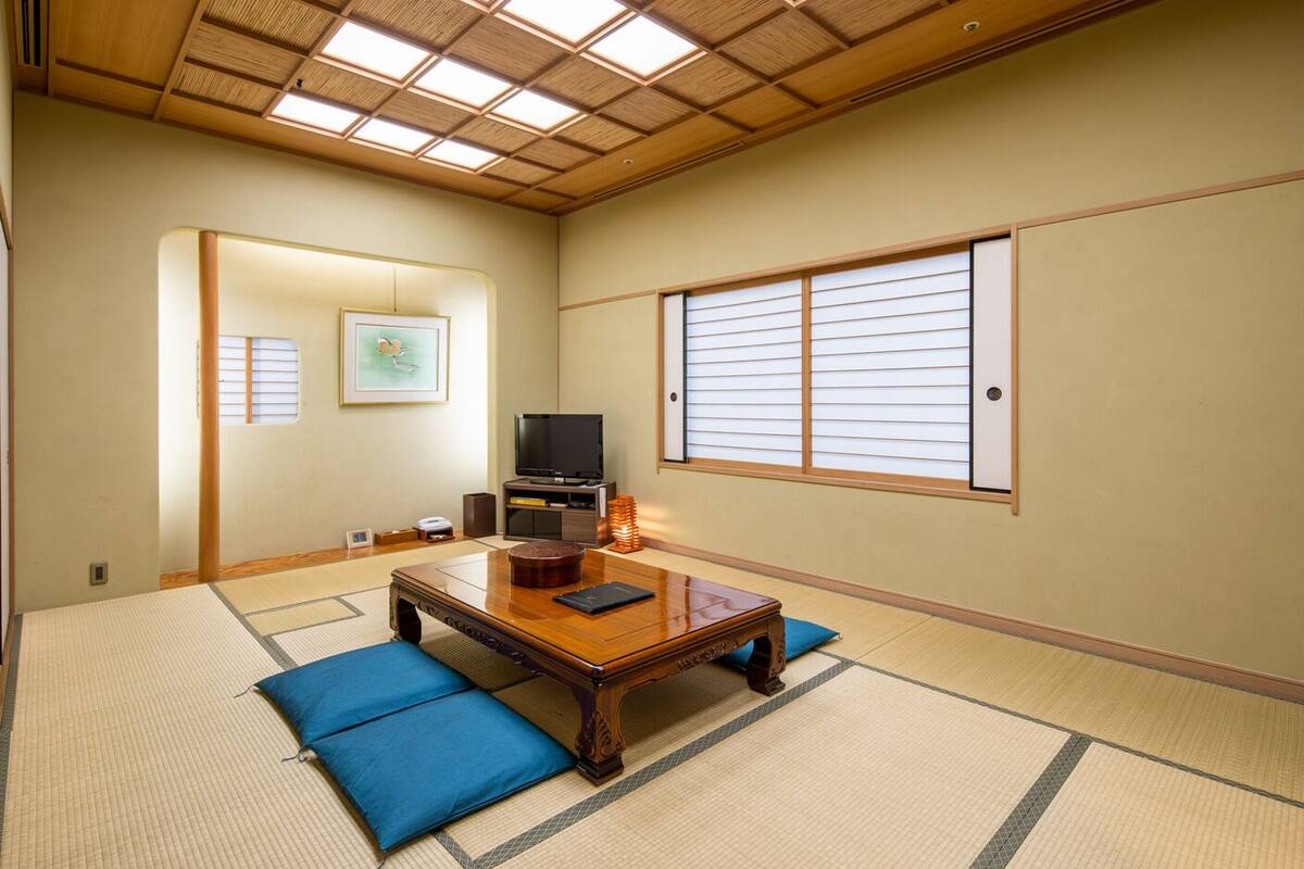 Une pièce de style japonais traditionnel, avec un sol recouvert de tatamis, une table en bois, un téléviseur et des paravents en papier.