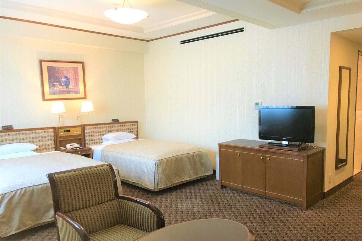 Une chambre d’hôtel avec deux lits, un téléviseur posé sur une commode, une chaise et une table.