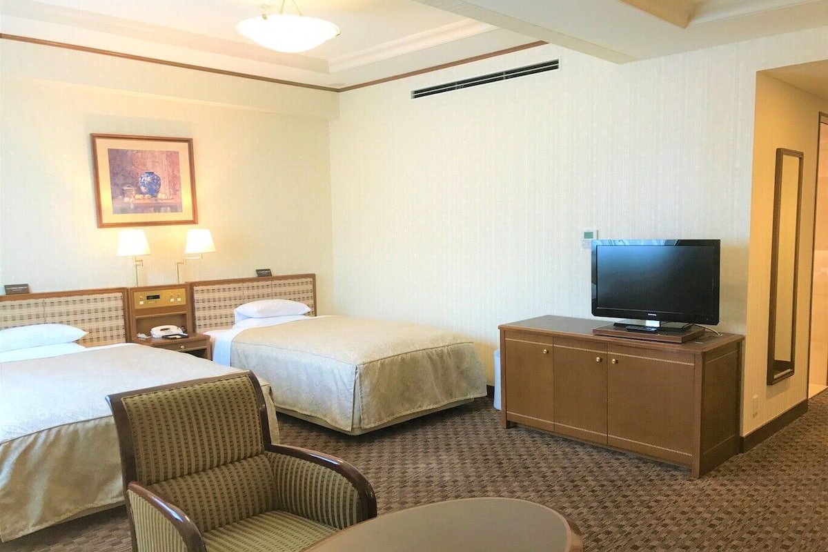 Une chambre d’hôtel avec deux lits, un téléviseur posé sur un meuble, une chaise et une petite table.