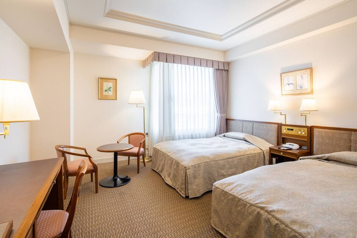 Une chambre d’hôtel avec deux lits, un bureau, une chaise, une lampe et une table de chevet avec un téléphone.