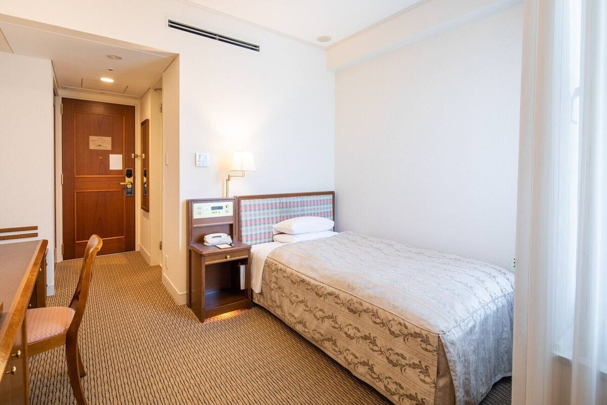 Une chambre d’hôtel comprenant un lit, un bureau, une chaise, une table de chevet et une lampe.