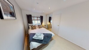 A neatly arranged bedroom with a bed, bedside tables, a mirror, and a wardrobe. - Victoria House (Hull)