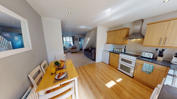 A modern kitchen with wooden cabinets, a dining area with a table and chairs, and a staircase leading to another level. - Victoria House (Hull)