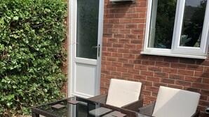A patio area with a glass-top table and wicker chairs, a white door, and a brick wall. - Victoria House (Hull)