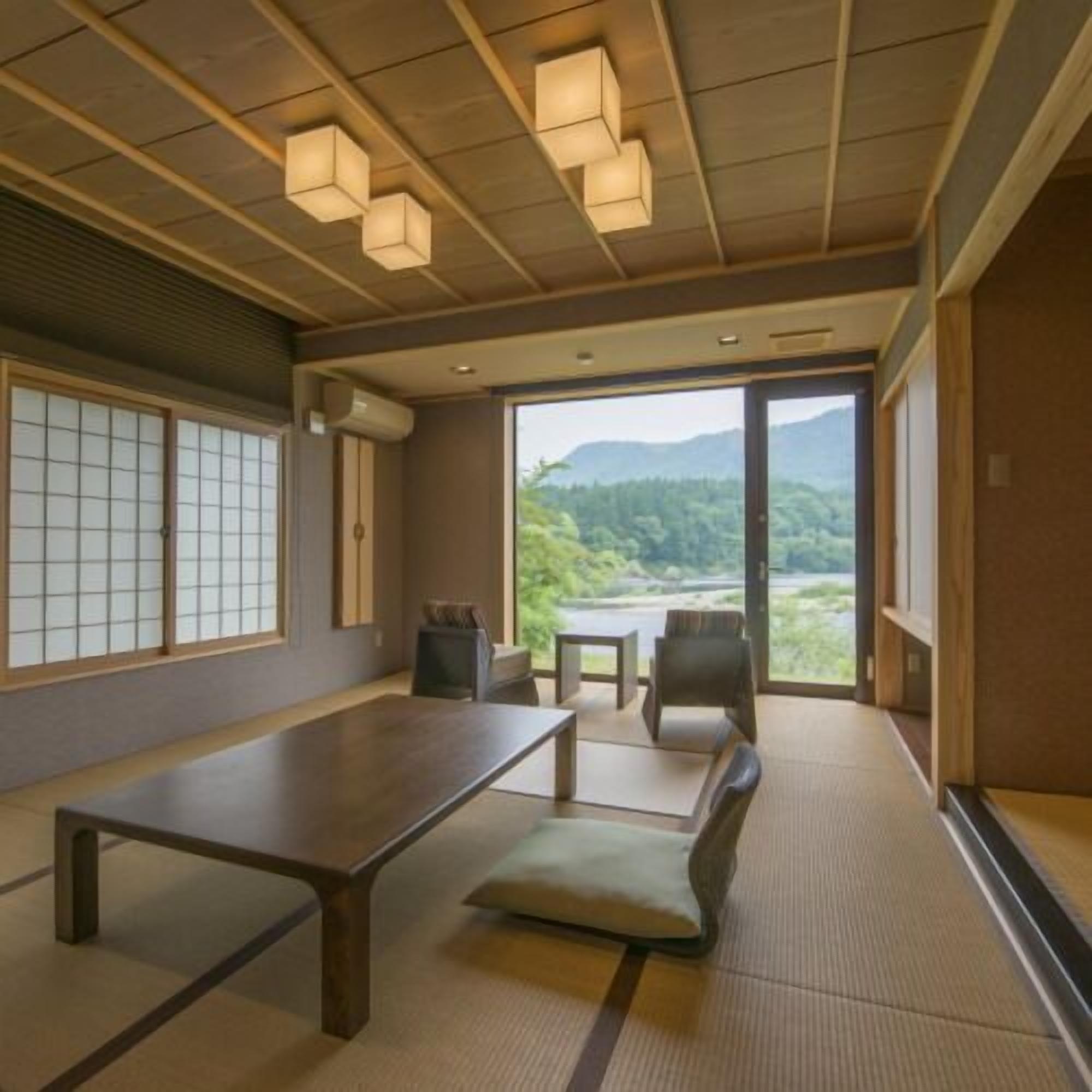 Una habitación con suelo de tatami, una mesa baja, un banco acolchado y vistas a un paisaje montañoso a través de amplios ventanales.