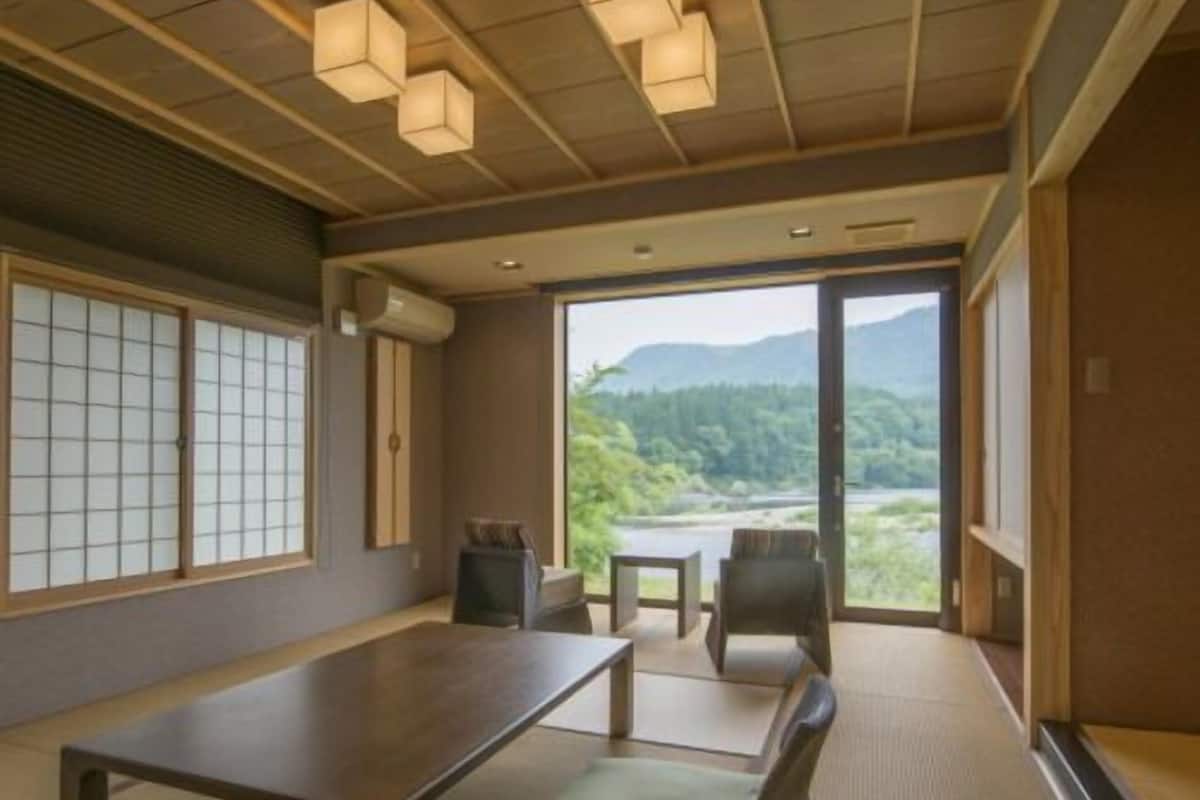 A room with tatami flooring, a low table, a cushioned bench, and a view of a mountainous landscape through large windows.