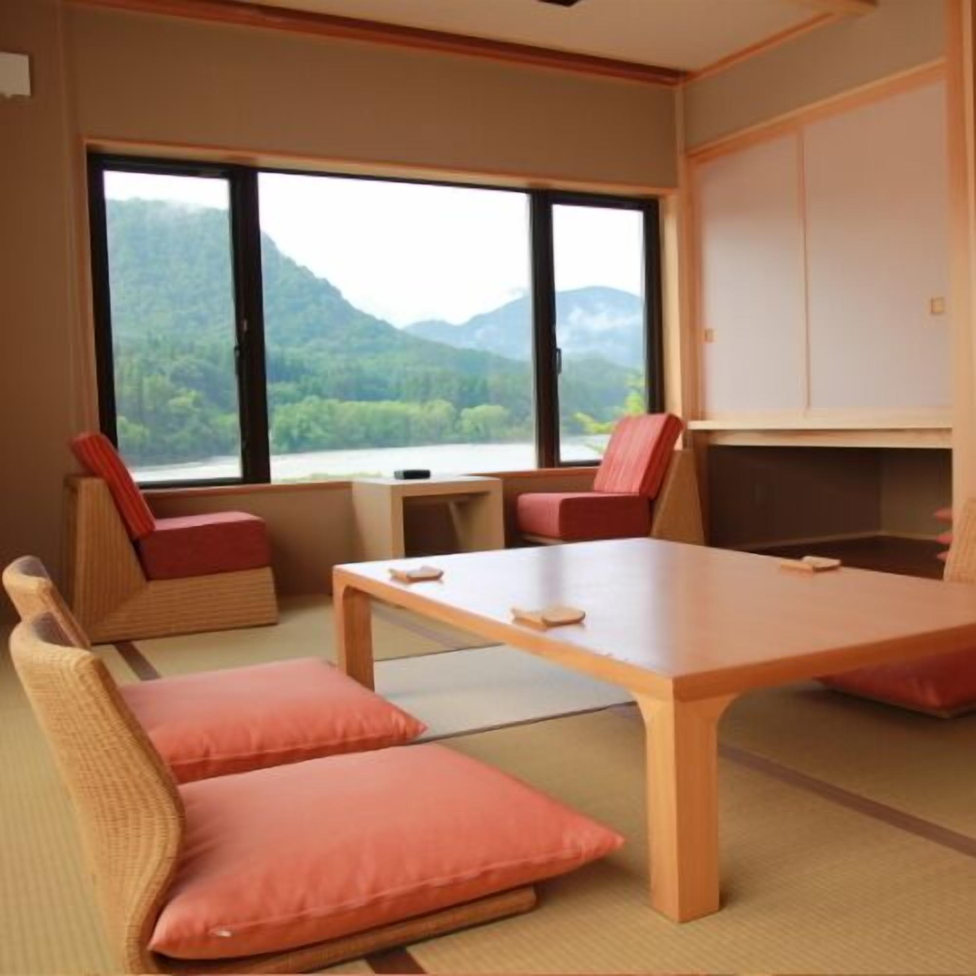 Una habitación con un ventanal grande, una mesa de madera y dos zonas de descanso con cojines.