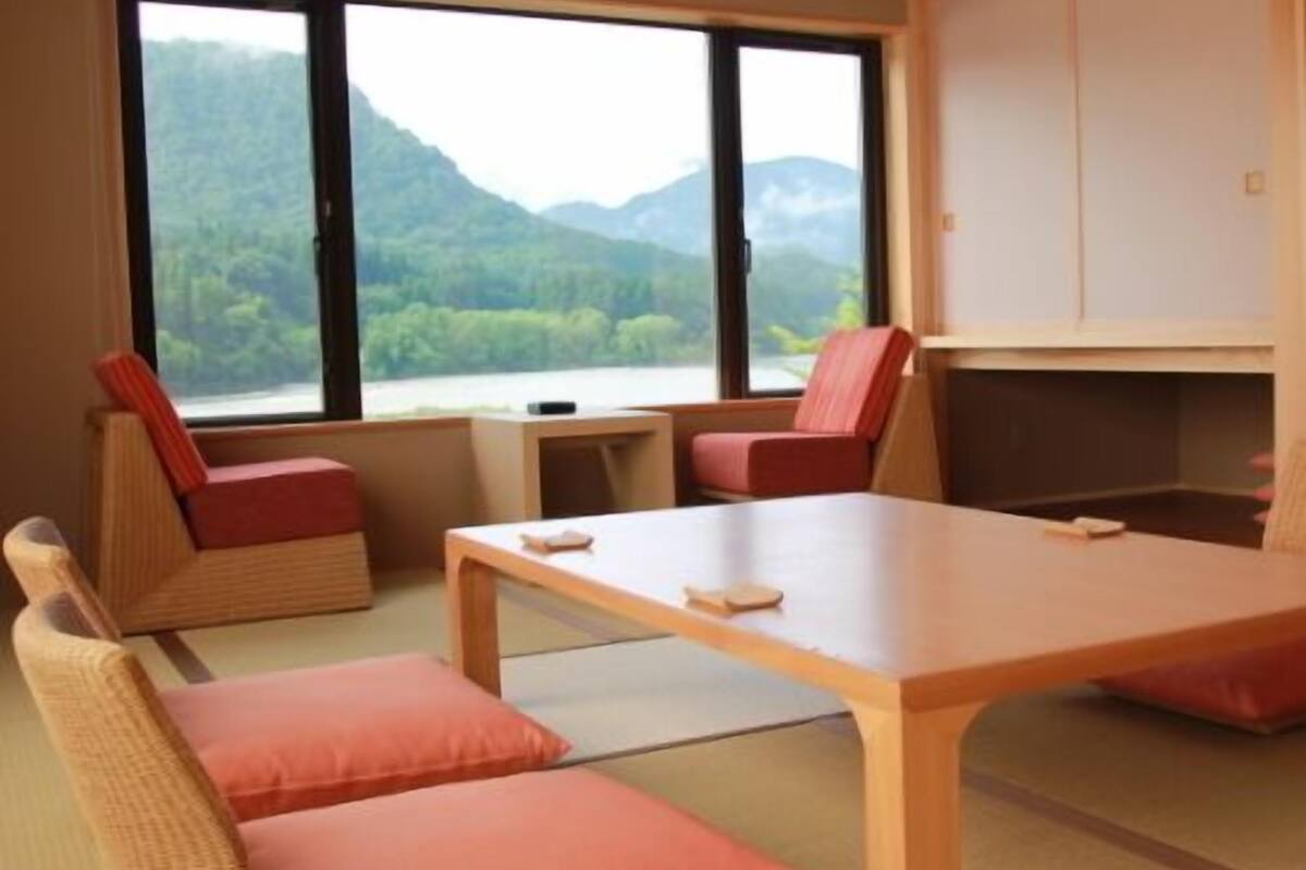 A room with a large window, a wooden table, and two cushioned seating areas.