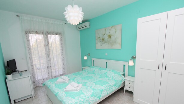 A bedroom with a bed, a nightstand, a TV, a wardrobe, and a window with curtains. - Rooms Petra (Rovinj)
