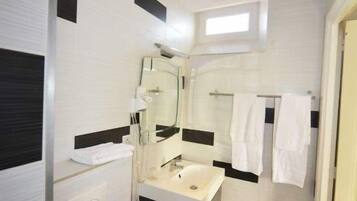 Une petite salle de bain avec un lavabo blanc, un miroir et des toilettes. On y trouve un porte-serviettes sur lequel sont suspendues des serviettes, ainsi qu’une petite fenêtre au-dessus du miroir.