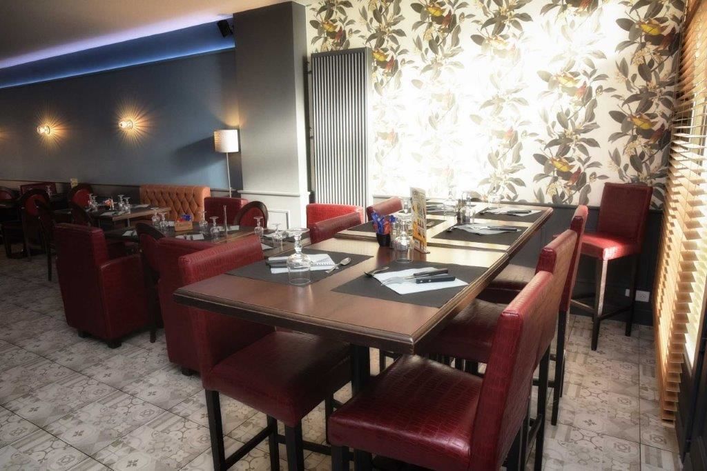 A restaurant with a long table, red upholstered booths, and patterned wallpaper.