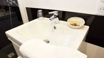 Un lavabo bianco con rubinetto cromato, un dispenser di sapone in vetro e un cesto di vimini con articoli da toilette.
