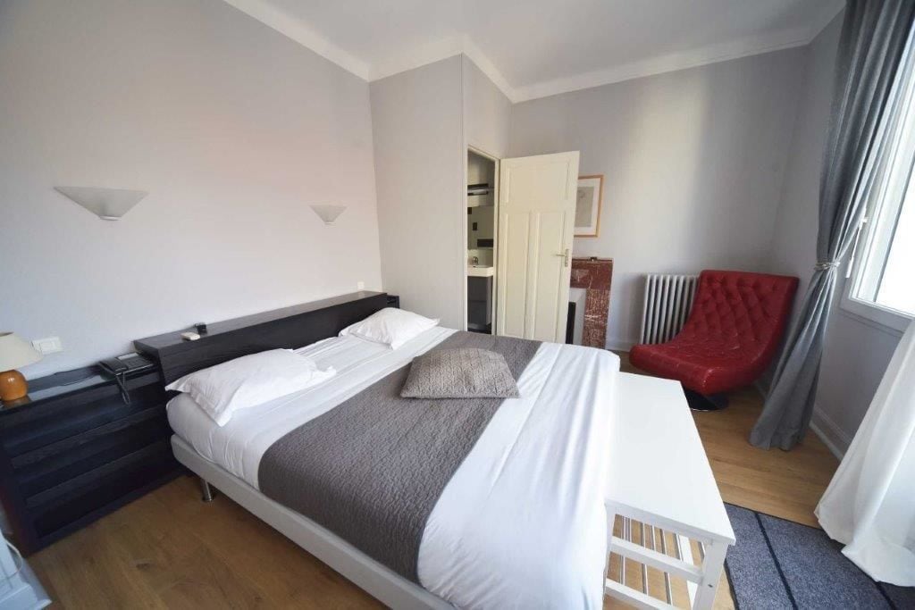 Una habitación de hotel con cama, mesita de noche y una silla roja.