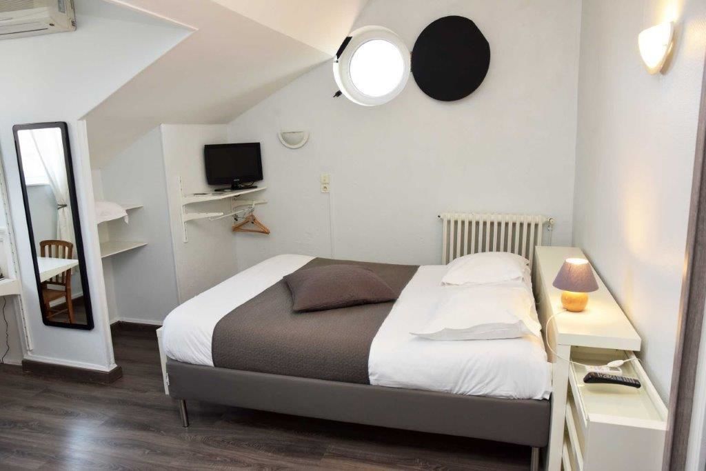 A bedroom with a bed, a desk, a TV, a mirror, a lamp, and a radiator.