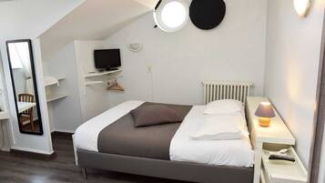 A bedroom with a bed, a desk, a TV, a mirror, a lamp, and a radiator.