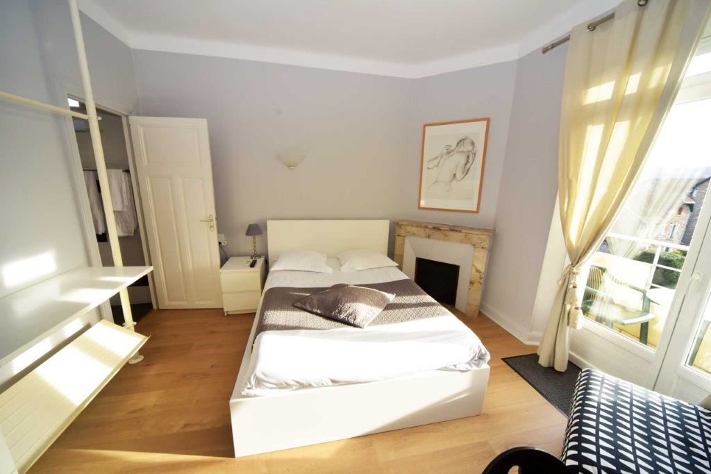 A bedroom with a bed, bedside tables, a wardrobe, a fireplace, and a window with curtains.