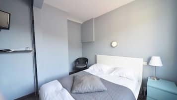 A hotel room with a bed, a chair, a bedside table with a lamp, and a wall clock.