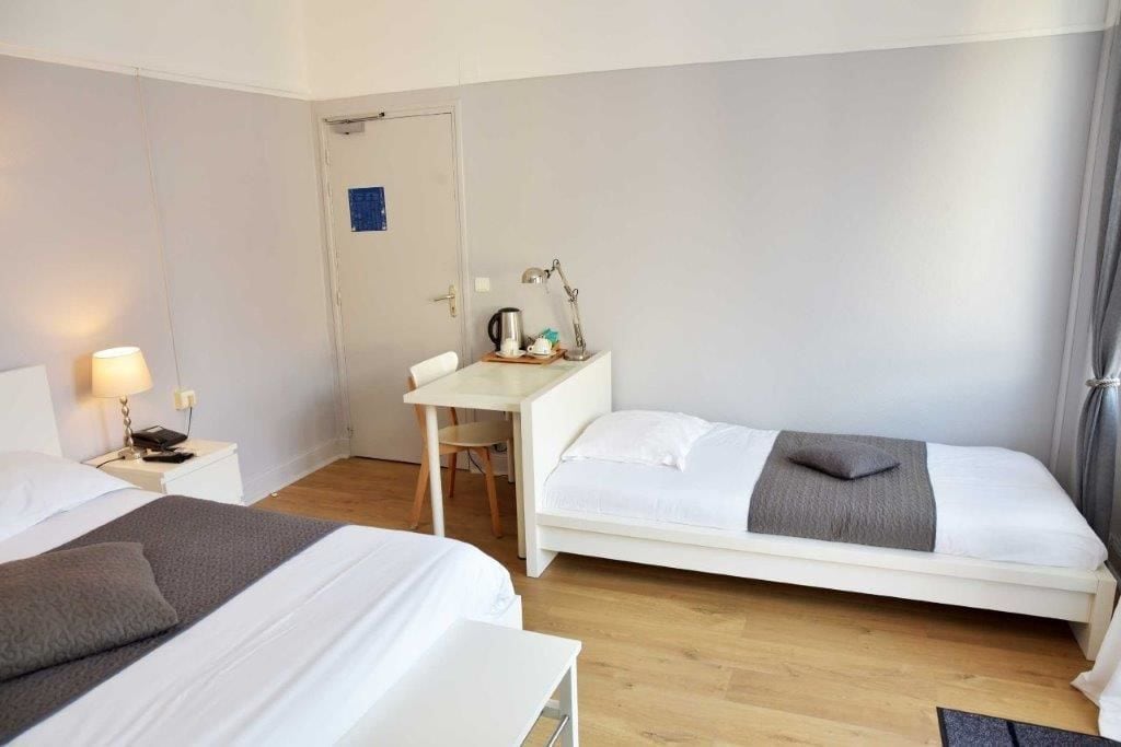 A hotel room with two beds, a desk with a chair, a coffee maker, and a door with a blue sign.