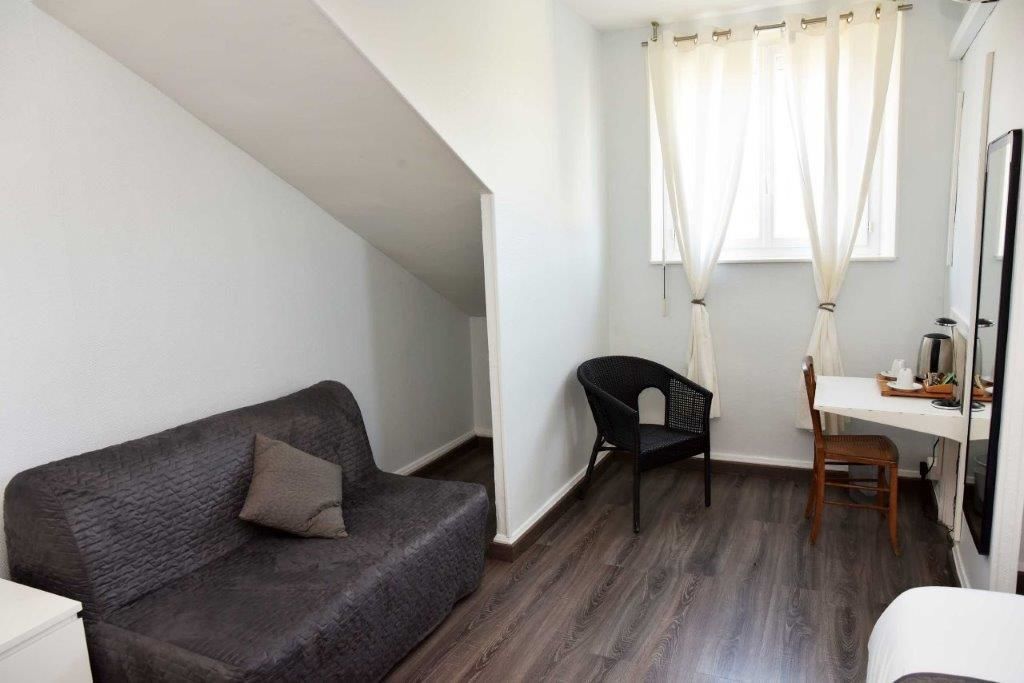 A room with a dark grey sofa, a black chair, a wooden desk, and a white chair.