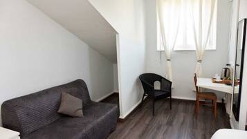 A room with a dark grey sofa, a black chair, a wooden desk, and a white chair.