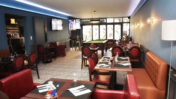 A restaurant with red upholstered booths and tables, a pool table, and a television screen.