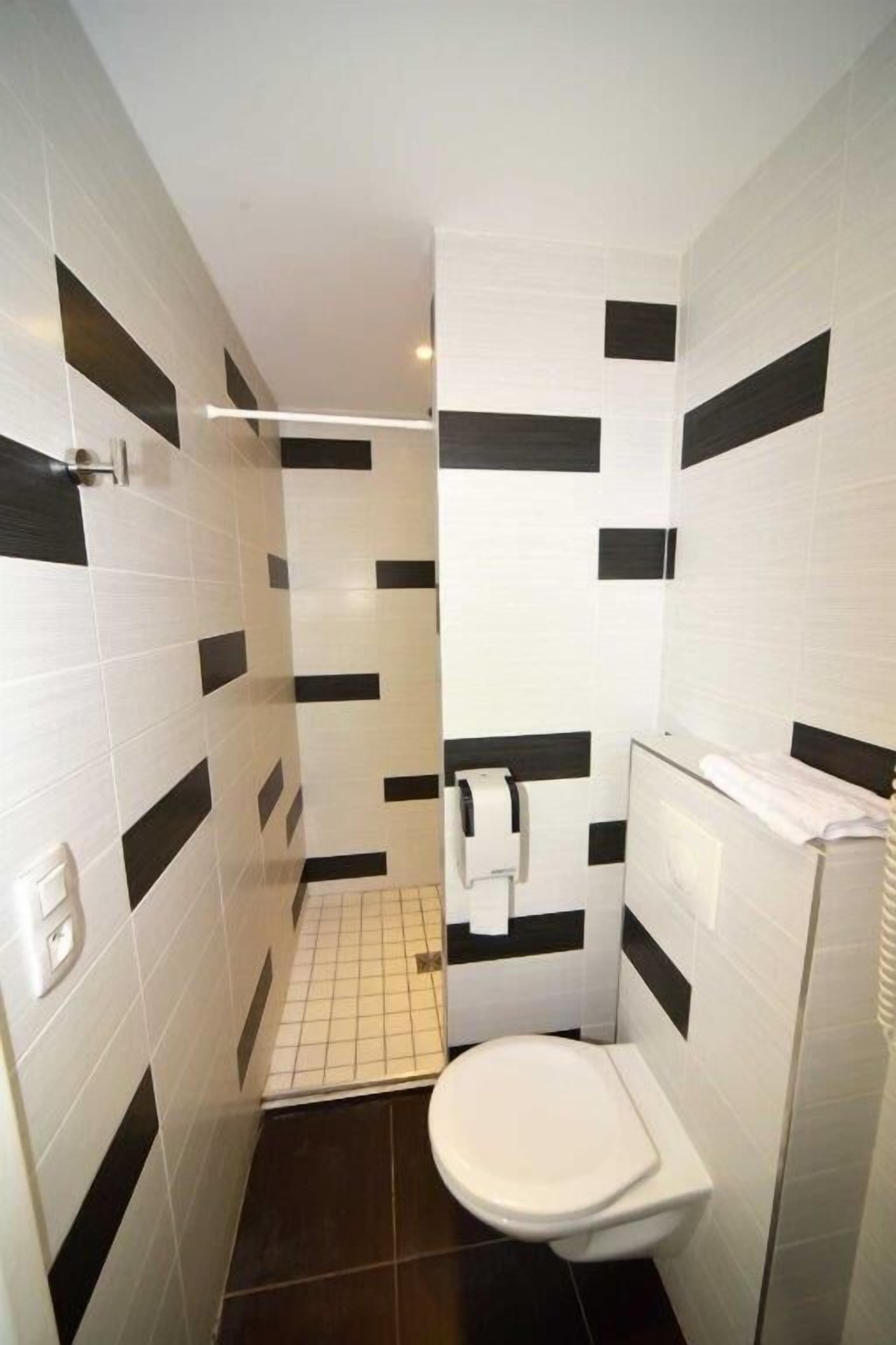 Een kleine badkamer met witte en zwarte tegels, een toilet en een douchehoek.