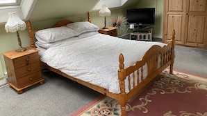 Un dormitorio con techo inclinado, una cama con cabecera de madera, una mesita de noche con lámpara, un aparador y un televisor sobre un soporte.
