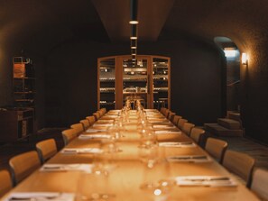 A long dining table with chairs, a wine rack in the background, and a staircase to the right. - Landgasthof (Riehen)