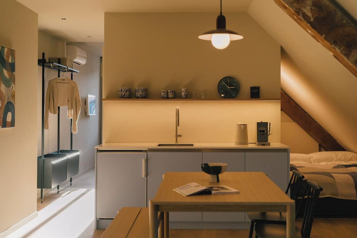 A compact kitchenette with a sink, a small refrigerator, and a clock on the wall.