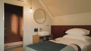 A bedroom with a bed, a bedside table, a mirror, and a window with curtains.