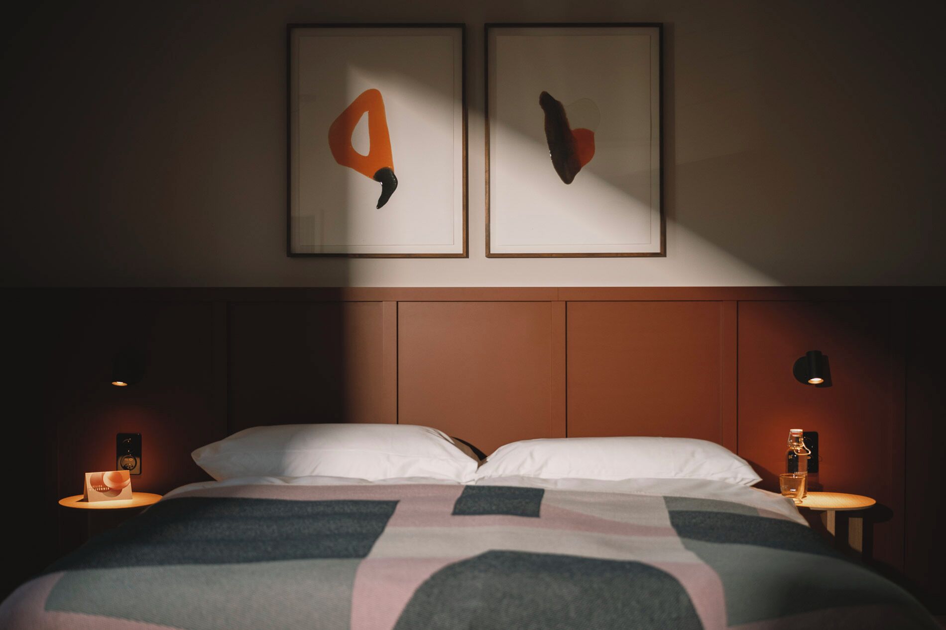 Una habitación de hotel con una cama, dos obras de arte en la pared y lámparas de noche.