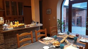 A dining area with a brick wall, wooden chairs, a table set for two with plates, cups, and a bread basket. - La Forge de l'Abbaye (Liessies)