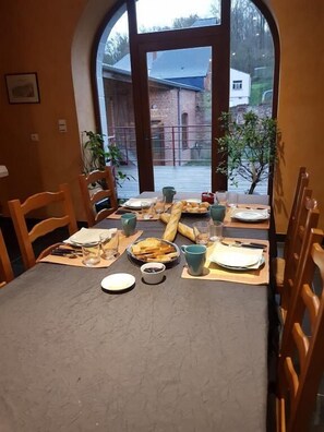 Mesa de comedor lista para dos con vista a un edificio de ladrillo y una casa blanca a través de un ventanal arqueado.
