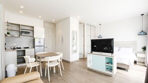 A modern apartment with a kitchenette, a dining area, a TV, and a bedroom.