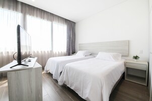 Habitación de hotel con dos camas, un escritorio con televisor de pantalla plana y una mesita de noche con una planta.