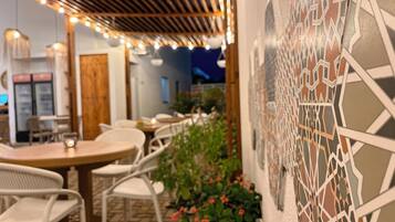 An outdoor seating area with tables and chairs, a patterned wall, and string lights.