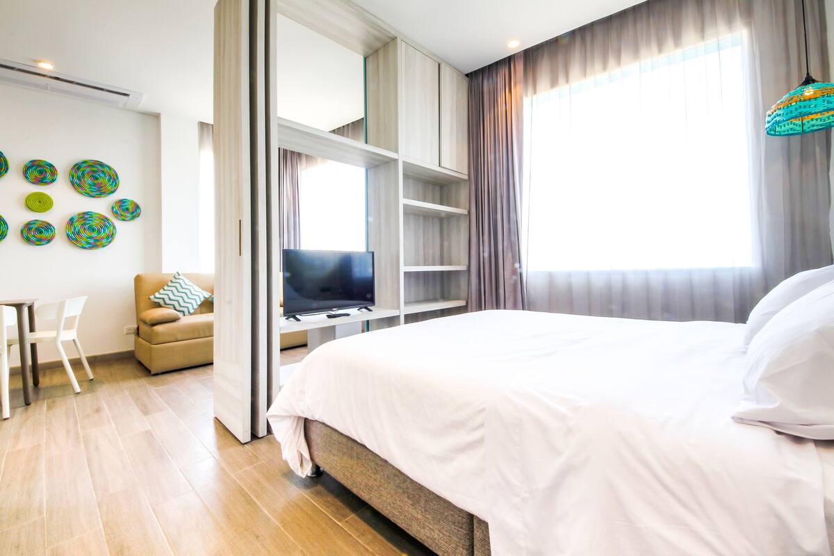 A modern hotel room with a large bed, a TV, a sofa, and a desk.