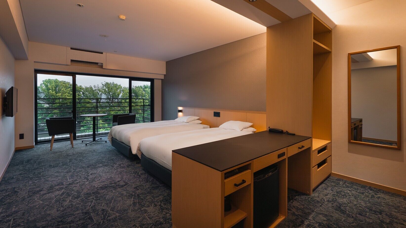 Een hotelkamer met twee bedden, een bureau, een stoel en een groot raam met uitzicht.