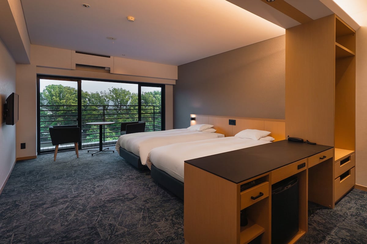 A hotel room with a large bed, a desk, and a chair. There is a balcony with a table and chairs.