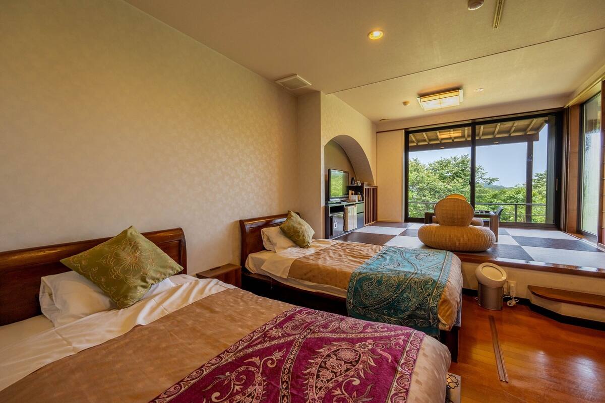 Una habitación de hotel con dos camas, televisión, ventana con vistas y balcón.