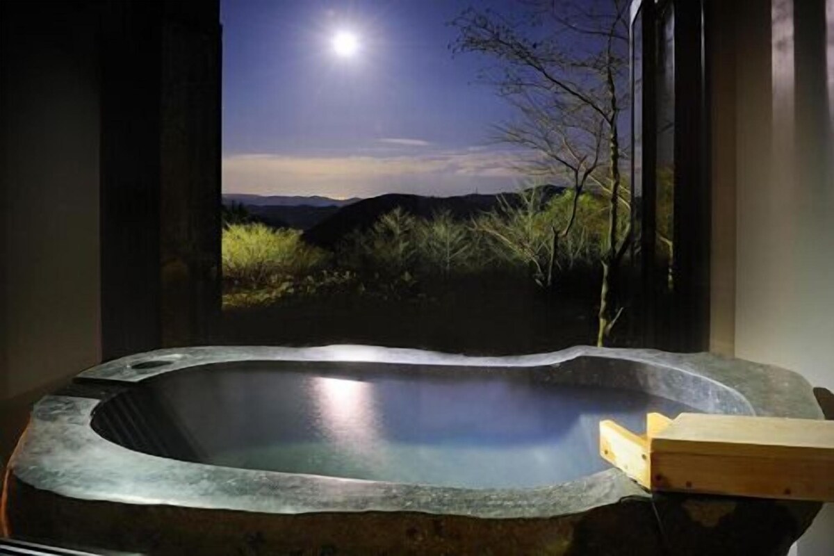 A hot tub with a view of a mountain landscape and a tree.