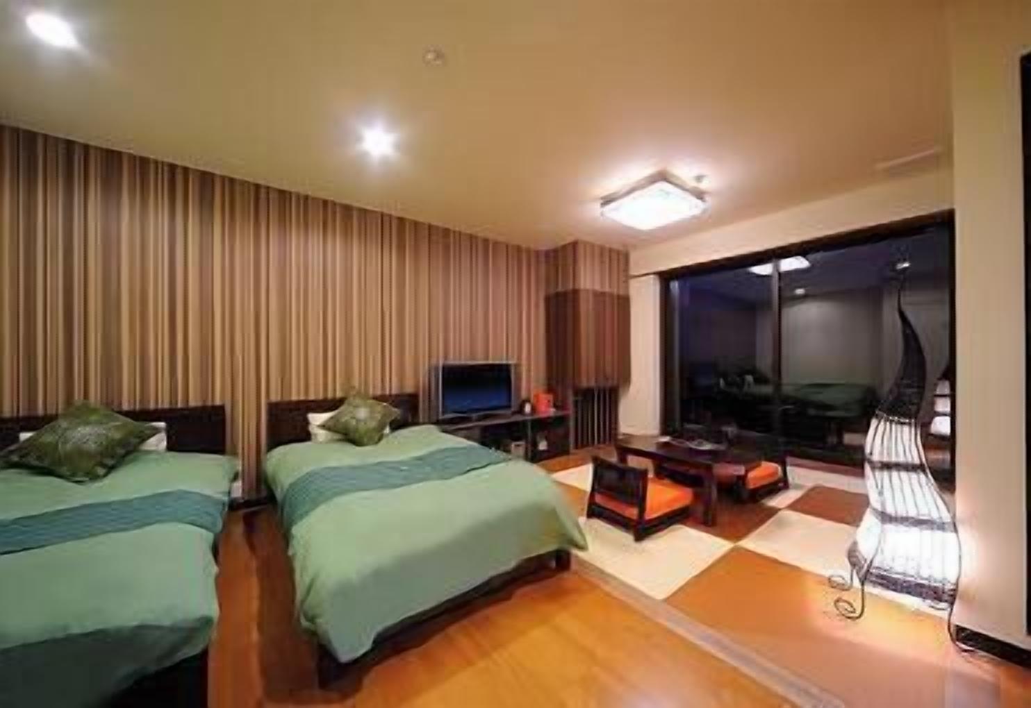 A hotel room with two beds, a TV, a desk, and a large window.